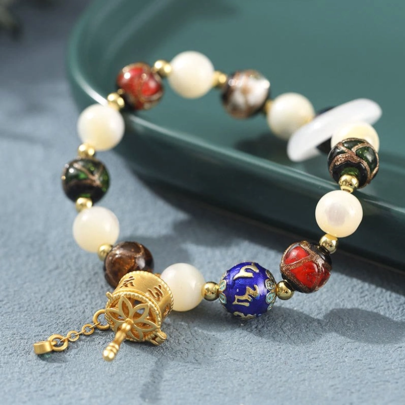 Close-up side view of Tibetan bracelet showing detailed gold prayer wheel charm and blue enamel mantra bead