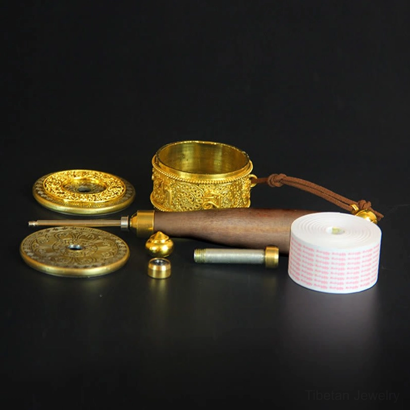 Disassembled Tibetan prayer wheel components showing brass metal barrel, natural wooden handle, decorative copper discs, and small brass bell