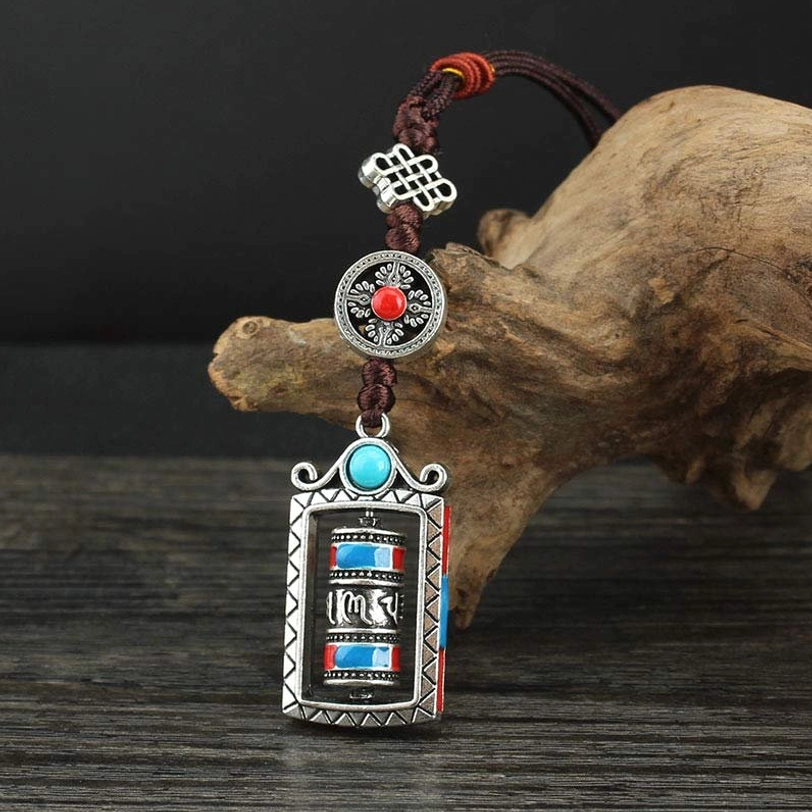 Tibetan prayer wheel keychain detail shot, intricate silver alloy work, Om Mani Padme Hum engraved design with traditional craftsmanship