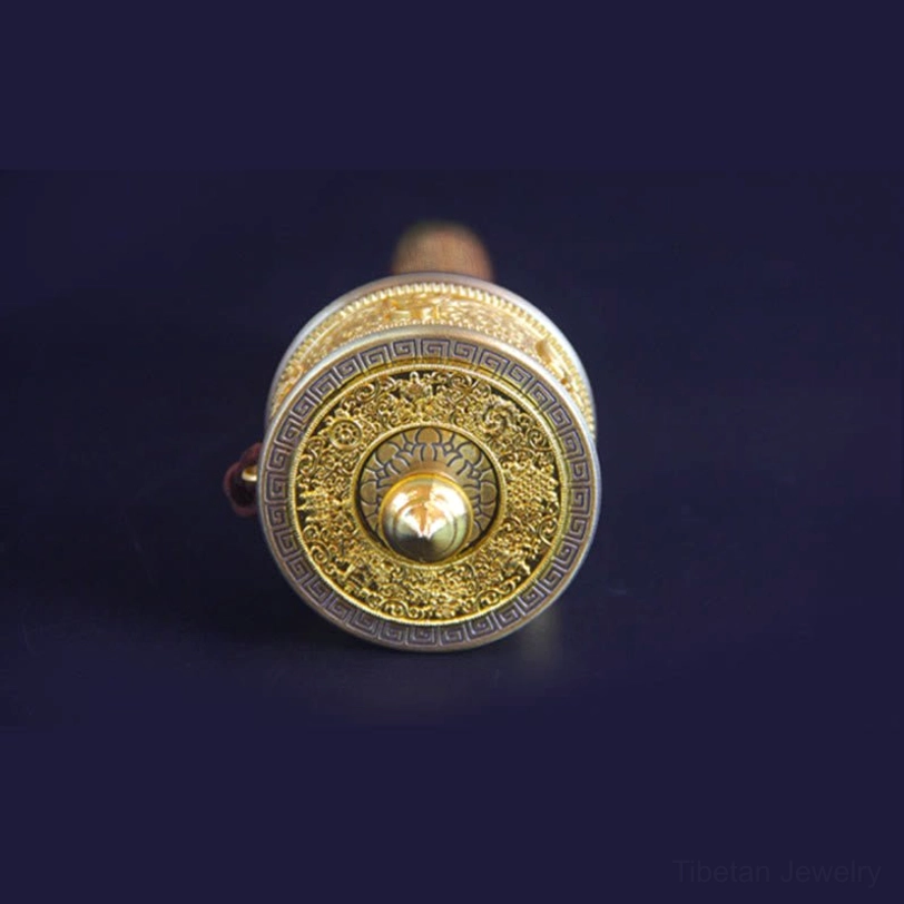 Rear top view of handmade prayer wheel showing round embossed end cap, brass decorative tip, and intricate carved metal texture details