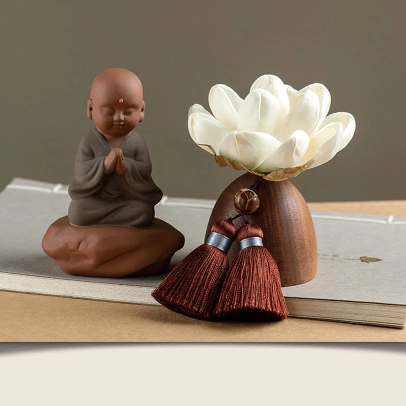 Praying little monk Buddha figurine in reverent pose with lotus flower and wooden base
