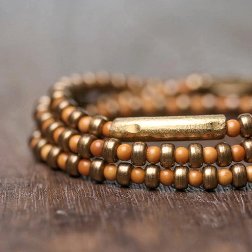 Side close-up view of handmade olive pit copper bracelet on wooden table with prominent brass tube accent detail