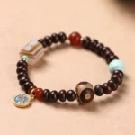 Purple Bodhi seed Dzi bead bracelet with yellow god of wealth amulet, striped agate, red agate, and turquoise beads on wooden surface