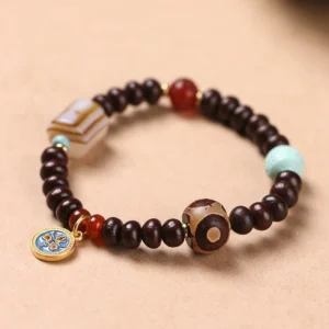 Purple Bodhi seed Dzi bead bracelet with yellow god of wealth amulet, striped agate, red agate, and turquoise beads on wooden surface