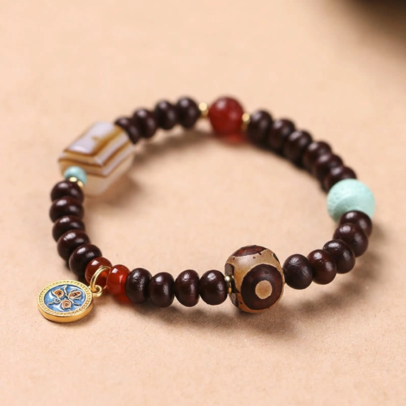 Purple Bodhi seed Dzi bead bracelet with yellow god of wealth amulet, striped agate, red agate, and turquoise beads on wooden surface
