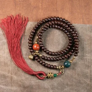 Purple bodhi seed 108 mala bracelet flat lay on wooden surface with red tassel and copper accents