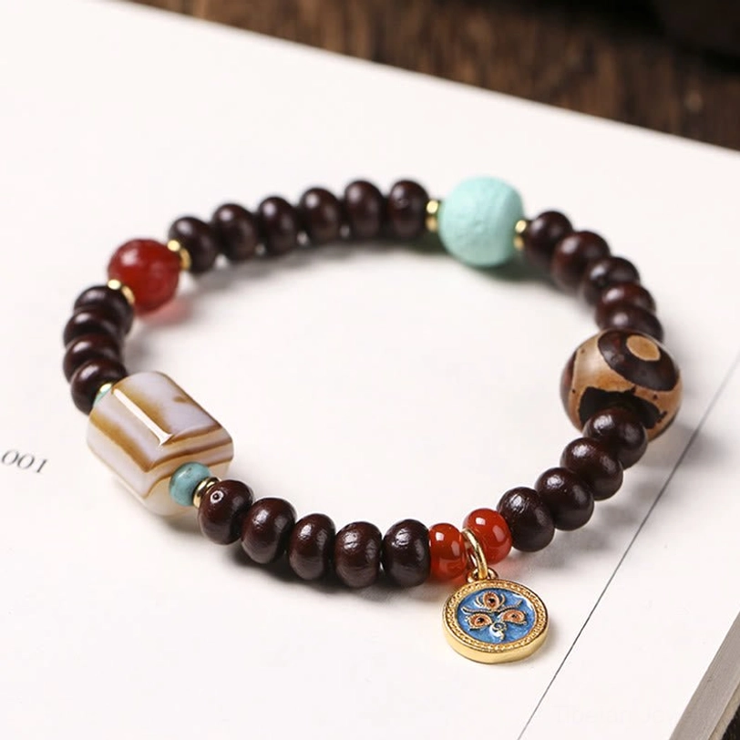 Purple bodhi seed bracelet with striped dzi bead, red agate beads, turquoise stone, and enamel pendant on kraft paper background