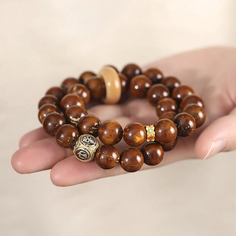 Close-up of Purple Gold Rat Bodhi seed beads on palm showing texture and reddish-brown color with metal charm