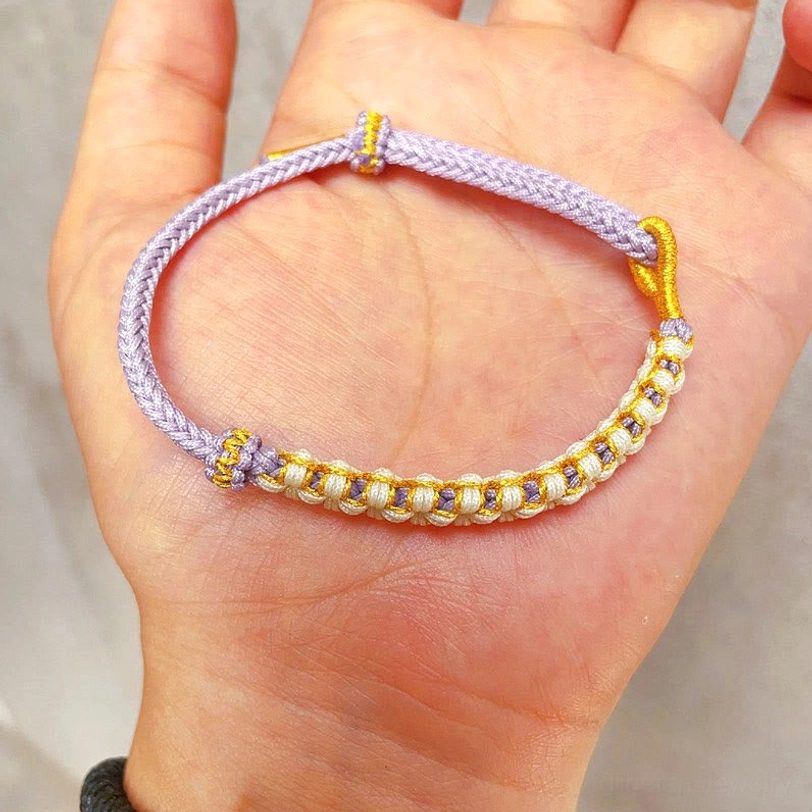 Purple Tibetan braided bracelet worn on palm showing peach blossom knot with gold metal details