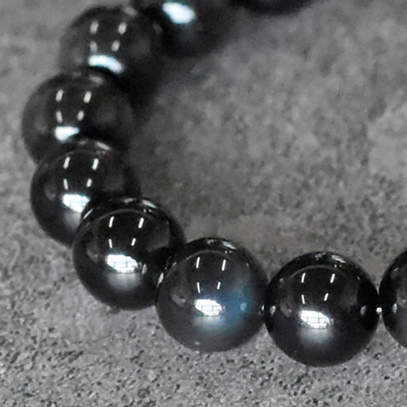 Rainbow Obsidian Beads Close-up - High Glossy Black Surface with Green-Blue Iridescent Glow on Concrete Background