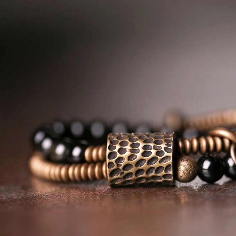 Close-up overhead view of rainbow obsidian double layer bracelet featuring bronze coil details, spacer beads, and polished black obsidian