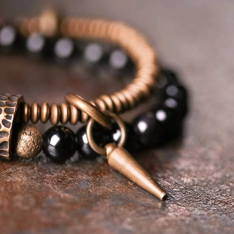 Detailed side view of double layered rainbow obsidian bracelet showing spike pendant, jump rings, hammered bronze coils, and healing beads