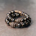 Rainbow obsidian copper healing bracelet top view flat lay showing glossy black beads with bronze metal charms