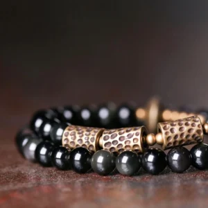 Side view of rainbow obsidian copper double wrap bracelet showing iridescent sheen on beads and aged vintage copper cylindrical ornaments, low-angle product photography