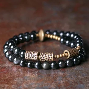 Rainbow obsidian double wrap bracelet with hammered copper accents displayed in top-down flat lay, showing polished black beads and vintage copper hardware on wooden surface