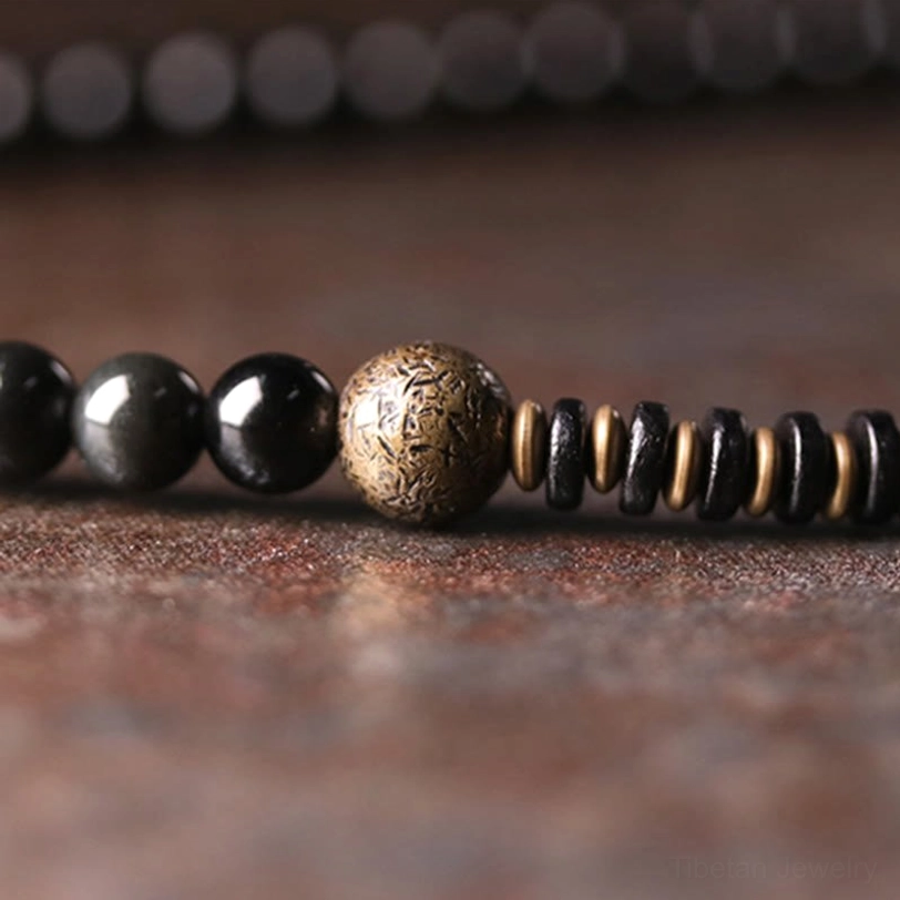Ebony wood and rainbow obsidian bracelet section featuring textured bronze focal bead with black beads and metal disc spacers