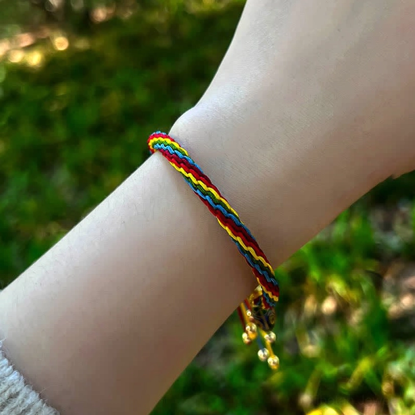 Simple rainbow woven Tibetan bracelet with gold tassel and bells worn on hand outdoors