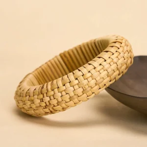 Bohemian rattan bangle three-quarter side view showing thick woven band and natural material texture on beige tabletop
