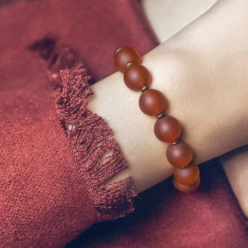 Red agate bracelet worn on wrist showing matte reddish-brown beads with simple elastic design close-up