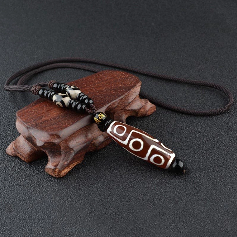 Red-brown nine-eye Dzi bead necklace with natural agate patterns and black spacer beads on wooden display stand, Tibetan spiritual pendant