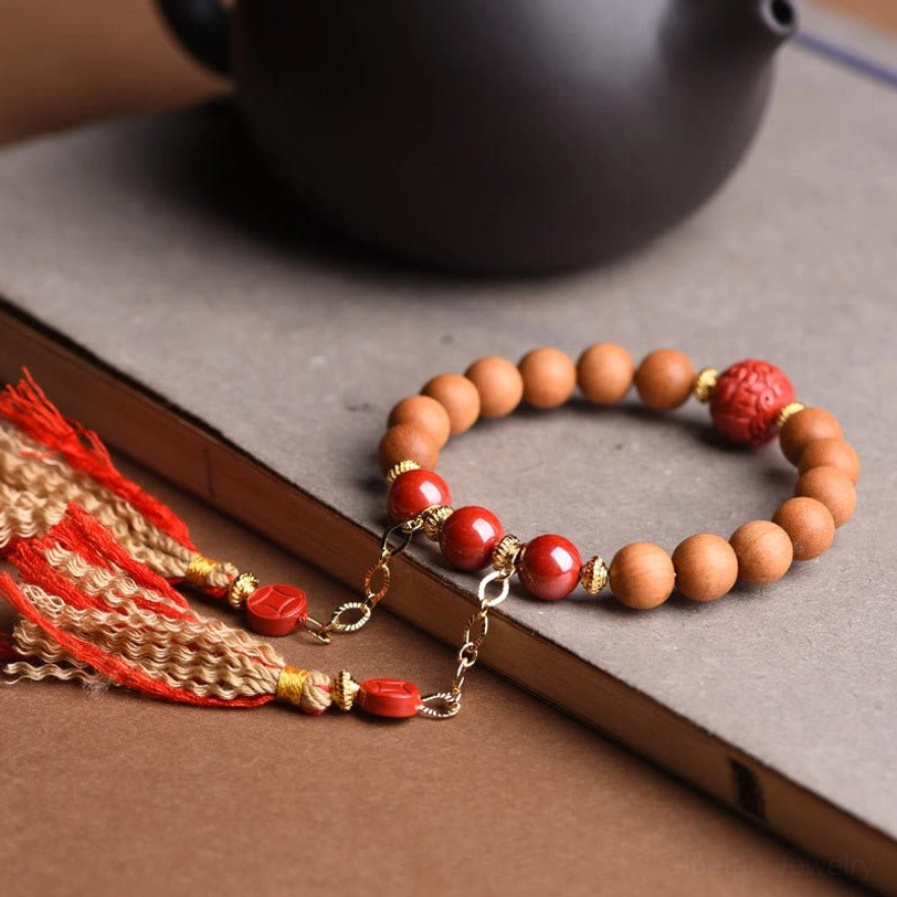 Tibetan cinnabar tassel bracelet with bright red beads and gold chain hardware displayed on book and black teapot background