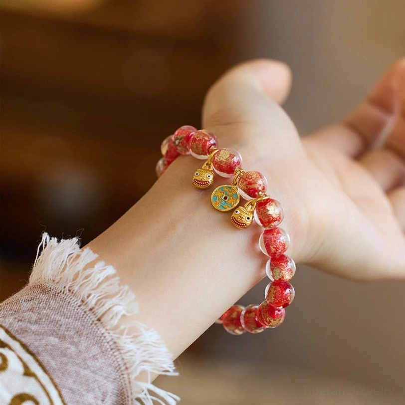 Red gradient liuli glass fortune bracelet with gold coin and Pi Xiu charms, side wrist-worn view