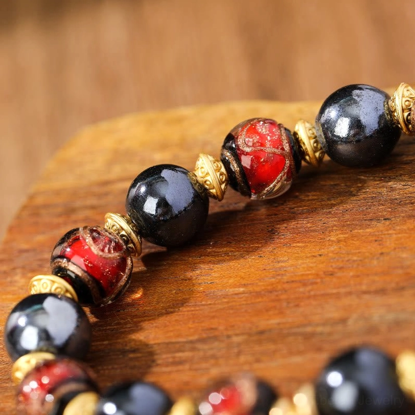 Swirled red liuli glass incense ash bracelet close-up detail with smooth dark beads and gold metal spacers