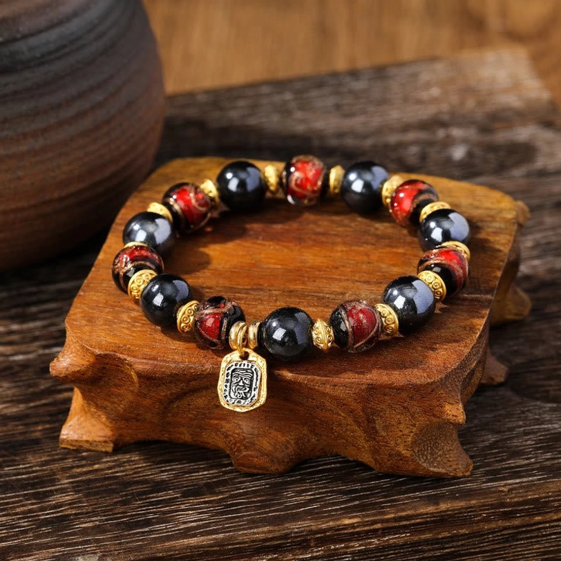 Red marbled liuli glass wealth bracelet with dark polished beads and gold accents on wooden stand
