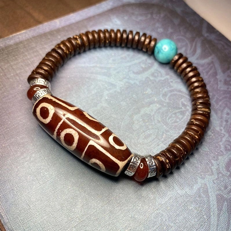 Red nine-eye dzi bead bracelet with white pattern, turquoise and red agate accent beads with metal spacers on dark gray background