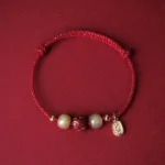 Red silk rope Hetian jade cinnabar lotus lucky bracelet with 14K gold plating, flat lay top-down view