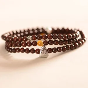 Triple wrap red sandalwood beaded bracelet with silver Fu charm and amber accent bead - side flat lay perspective