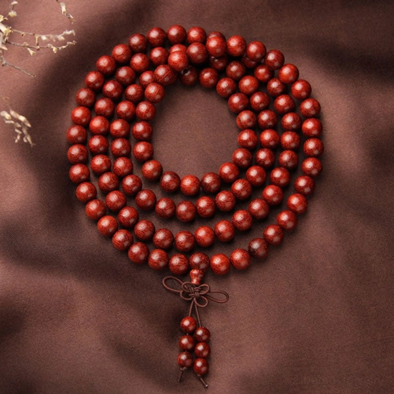 Circular 108 bead red sandalwood mala flat lay on dark brown fabric, showing neatly strung round wood beads with lower tassel pendant