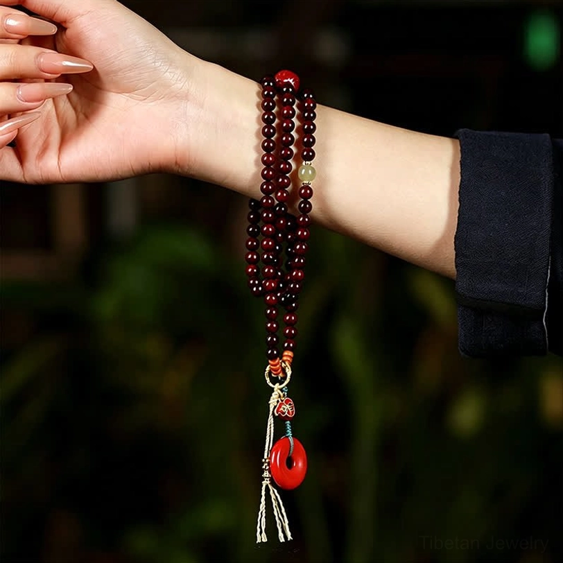 Red sandalwood mala prayer beads worn on wrist, close-up side view showing bead texture and peace buckle