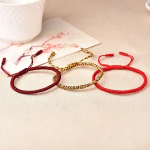 Minimalist adjustable red string bracelets with sliding knot closure displayed on table with teacup and decorative card