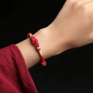 Red string protection bracelet worn on wrist showing adjustable knot and jade bead design