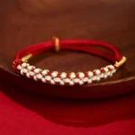 Red Tibetan peach blossom knot braided bracelet with gold thread accents on wooden tray
