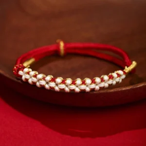 Red Tibetan peach blossom knot braided bracelet with gold thread accents on wooden tray