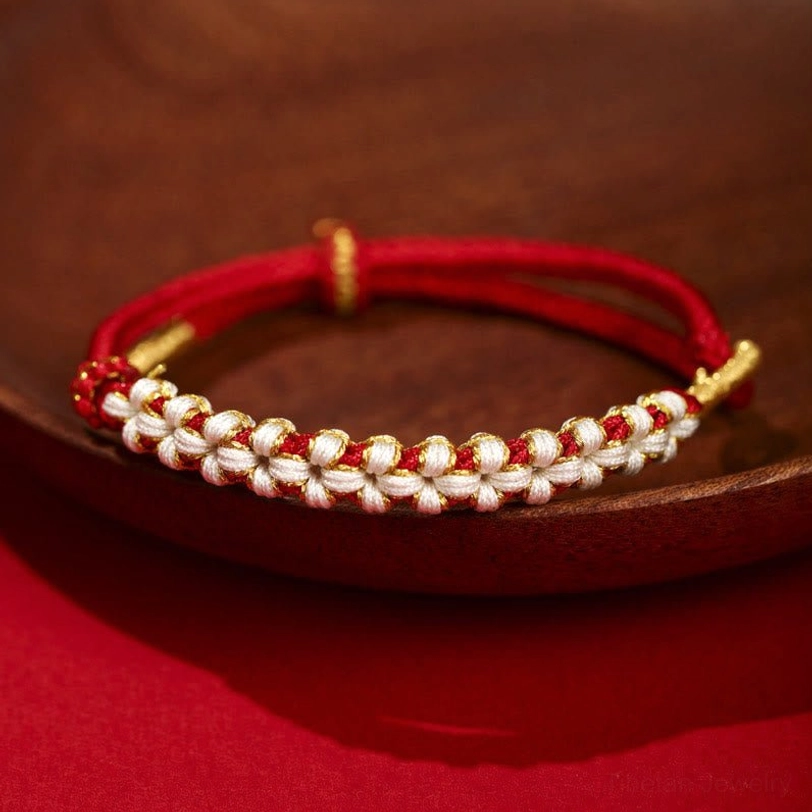 Red Tibetan peach blossom knot braided bracelet with gold thread accents on wooden tray