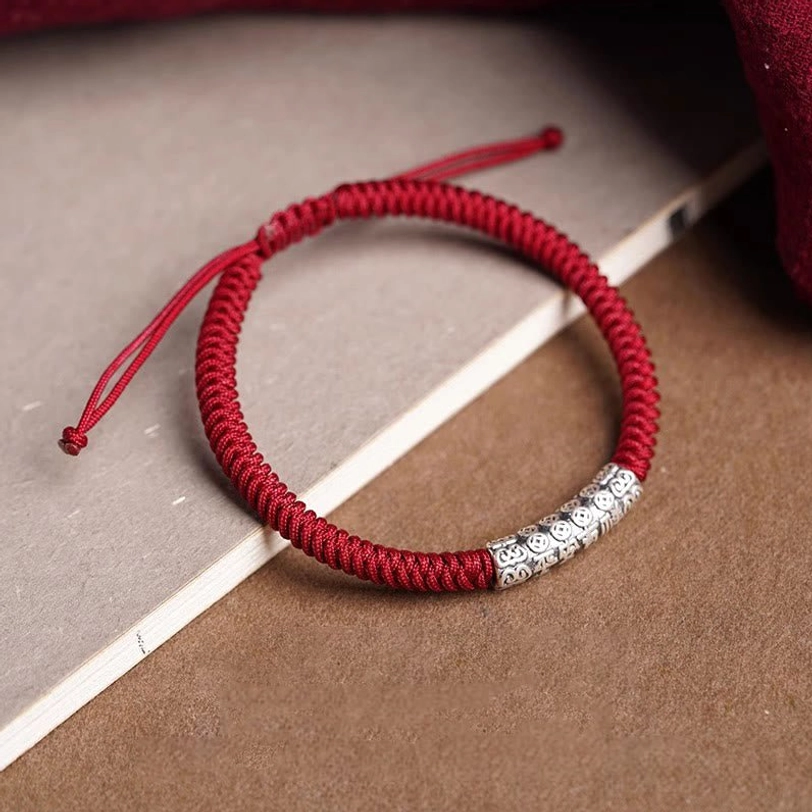 Red braided Tibetan cord bracelet with sterling silver engraved bead, side flat view on wooden background