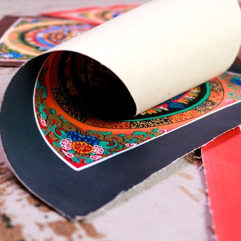 Rolled Tibetan mandala thangka showing floral decorative borders and cream paper with black underlayer