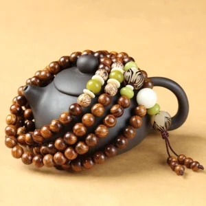Rosewood prayer mala set photographed from side angle on black ceramic teapot, displaying natural wood grain and woven tassel details