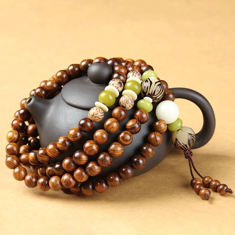 Rosewood prayer mala set photographed from side angle on black ceramic teapot, displaying natural wood grain and woven tassel details