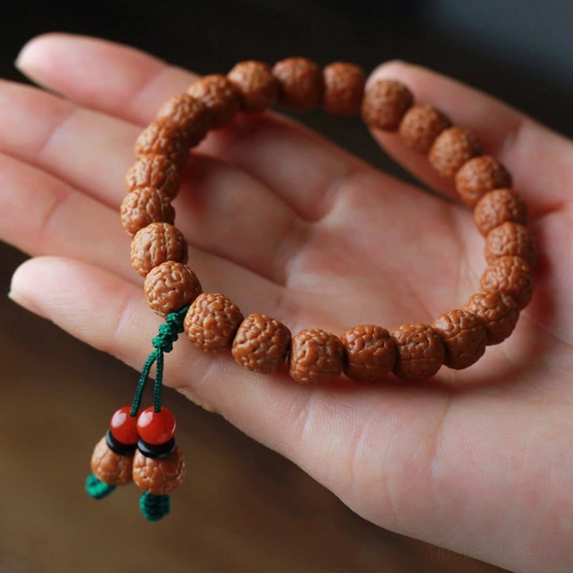 Hand-held close-up of rudraksha bodhi seed bracelet with textured beads and red agate tassel