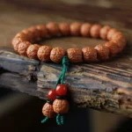 Rudraksha bodhi seed wealth bracelet with red agate tassel close-up view on wooden surface
