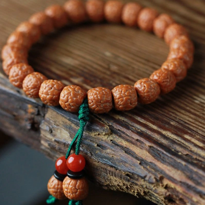 Rudraksha bodhi seed bracelet with textured beads and green cord on weathered wood background