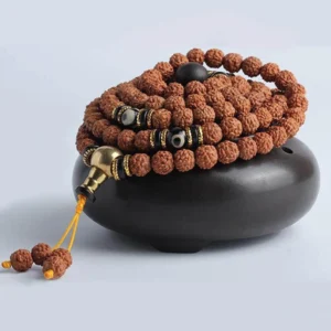Coiled rudraksha mala prayer bracelet with golden metal guru bead and black dzi spacer beads on dark ceramic - side view