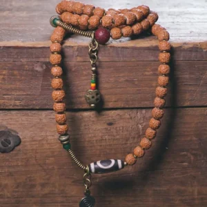 Authentic Rudraksha prayer mala bracelet featuring hand-painted Dzi Bead, metal spacers, and hanging charm on wooden background