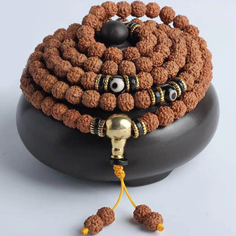 Rudraksha mala prayer bracelet coiled display with golden guru bead, black dzi details, and yellow hanging tassel on ceramic