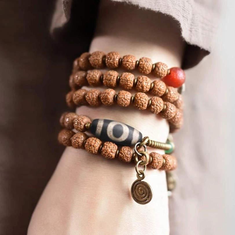 Multi-loop Rudraksha Mala Bracelet worn on wrist with Nine-Eye Dzi Bead and decorative spiral tassel with red accent