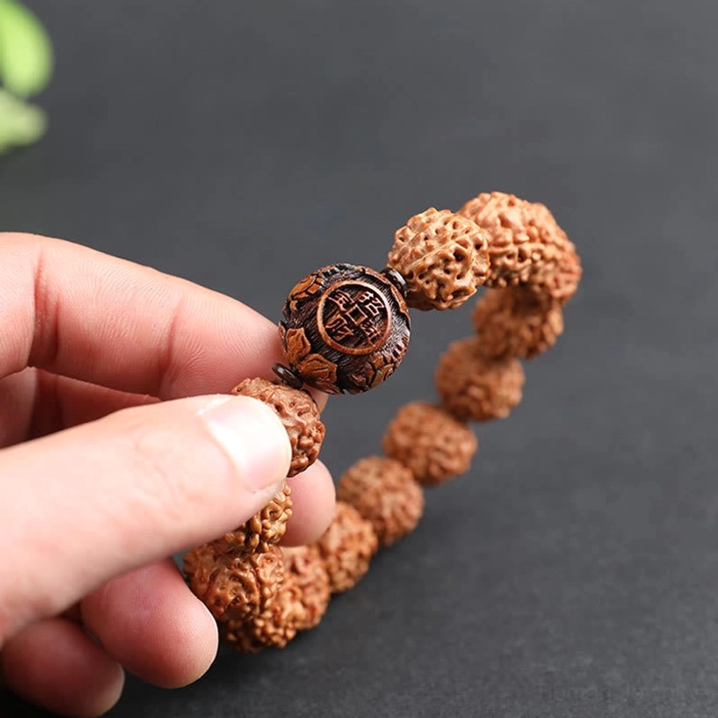 Hands holding Rudraksha Pixiu bracelet close-up, carved wooden accent bead detail visible, tactile perspective